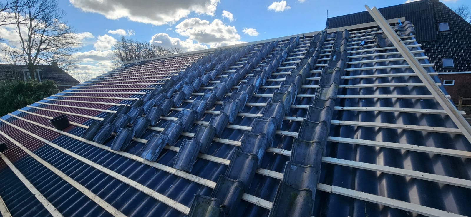 Pannendak in renovatie met tengels en panlatten onder blauwe lucht